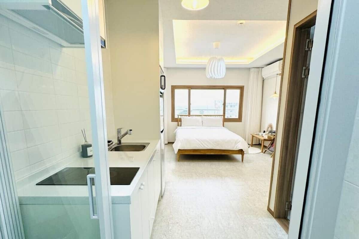 Une chambre à coucher moderne avec un grand lit, une fenêtre et une salle de bain équipée d’un lavabo et d’un miroir.