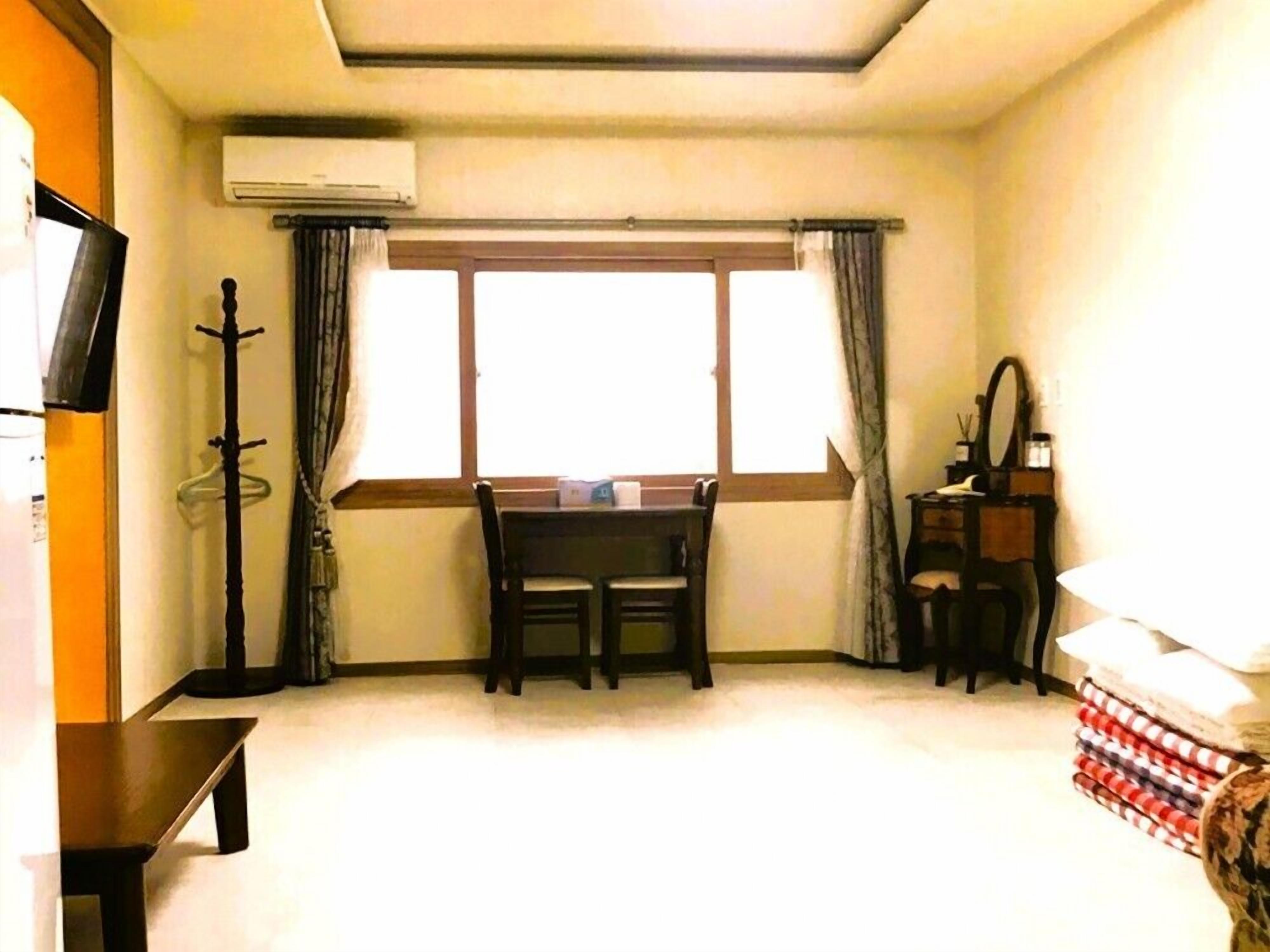 Una habitación con una mesa de comedor, sillas, un televisor, un espejo y una ventana con cortinas.