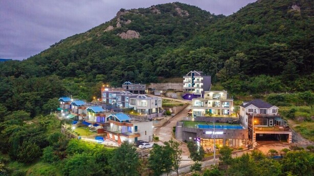 A residential area with modern houses, a swimming pool, and a hillside backdrop. - Heart Blue Road Town Pension (Yeongdeok)