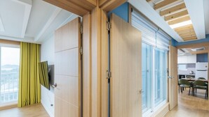 A modern room with wooden flooring, a large sliding glass door, and a view of a cityscape. - Heart Blue Road Town Pension (Yeongdeok)