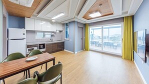 A modern kitchen with white cabinets, a wooden dining table, and a large window with a view. - Heart Blue Road Town Pension (Yeongdeok)