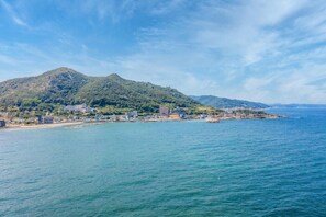 A coastal town with a mountain in the background, a beach, and a clear blue sky.
