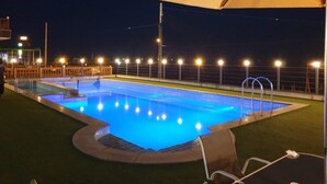 A nighttime swimming pool with illuminated edges, surrounded by a fence and a canopy. - Heart Blue Road Town Pension (Yeongdeok)
