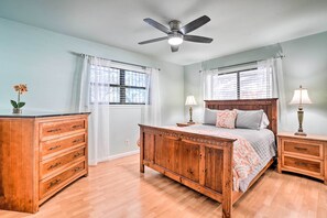 Quarto com cama de madeira, mesas de cabeceira, cômoda e ventilador de teto.