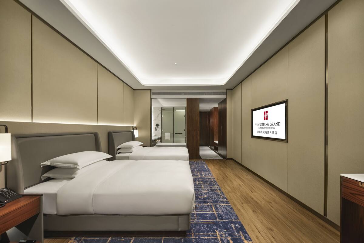 Habitación de hotel con dos camas, un escritorio, una lámpara, un televisor y un cartel con el nombre del hotel.