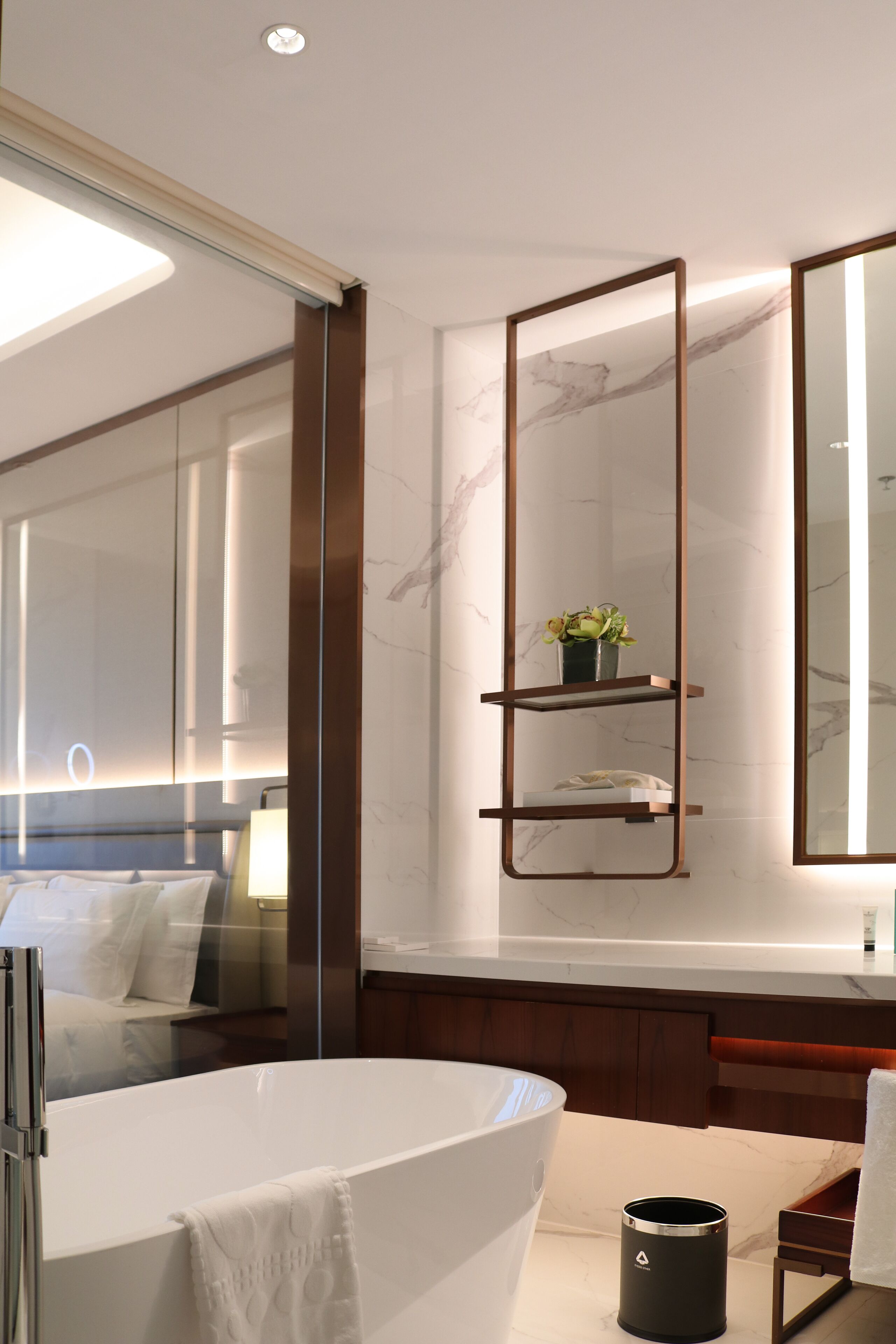 A modern bathroom with a large bathtub, a wooden shelf with a potted plant, and a large mirror.