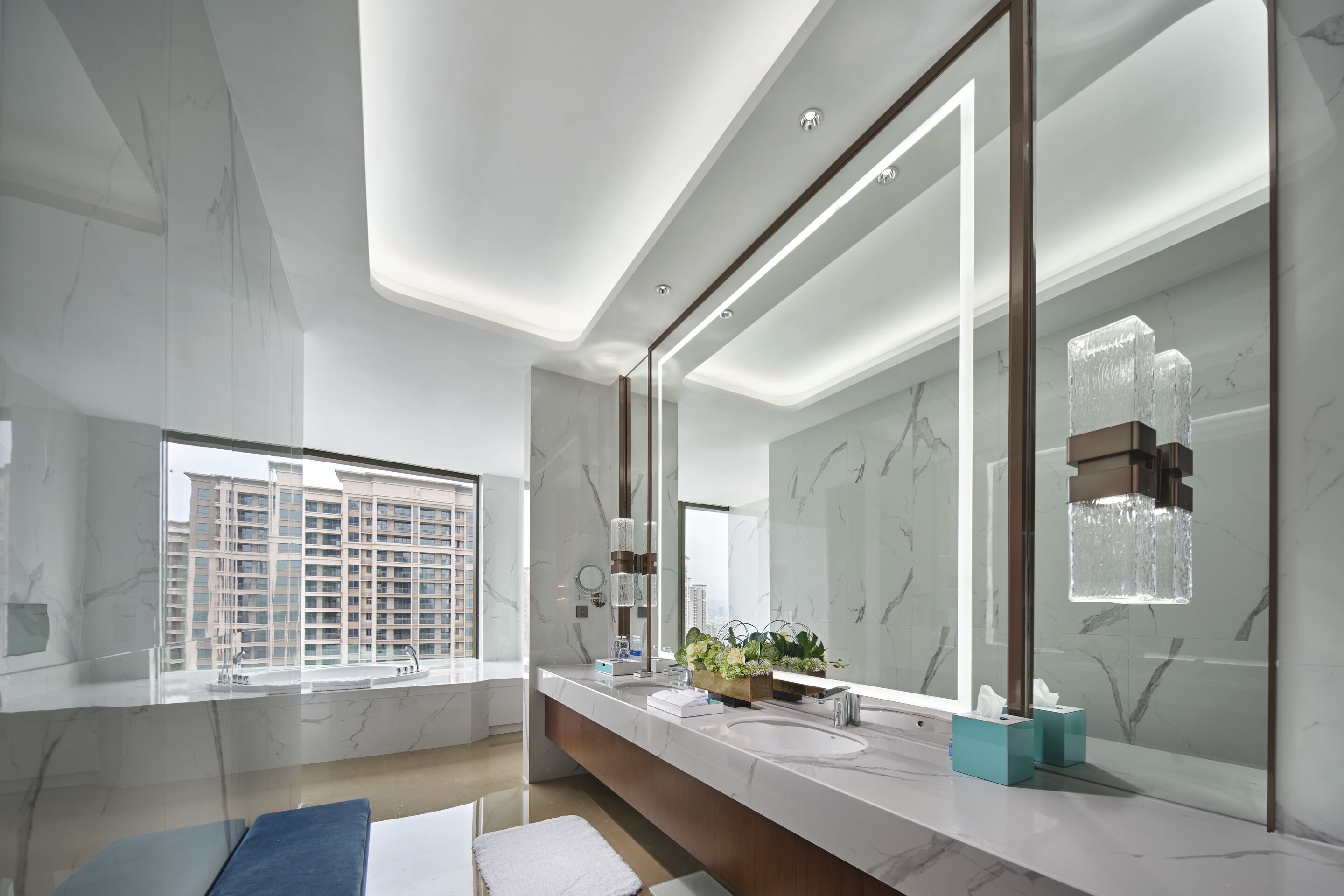 A modern bathroom with a large mirror, marble walls, and a window with a city view.