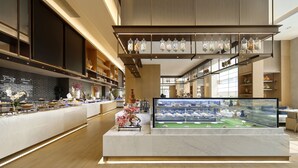 A modern hotel lobby with a marble reception desk, a glass display case with desserts, and a decorative plant arrangement. - Yuanchang Grand Harbourview Hotel (Quanzhou)