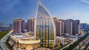 A modern hotel with a distinctive curved glass facade, surrounded by high-rise buildings and a busy road. - Yuanchang Grand Harbourview Hotel (Quanzhou)