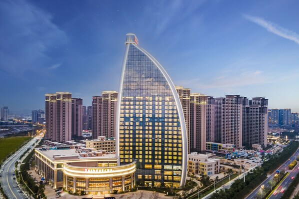 A modern hotel with a distinctive curved glass facade, surrounded by high-rise buildings and a busy road. - Yuanchang Grand Harbourview Hotel (Quanzhou)