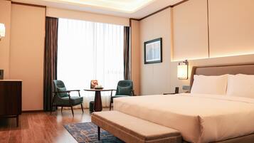 A hotel room with a large bed, two chairs, a small table, and a bench.