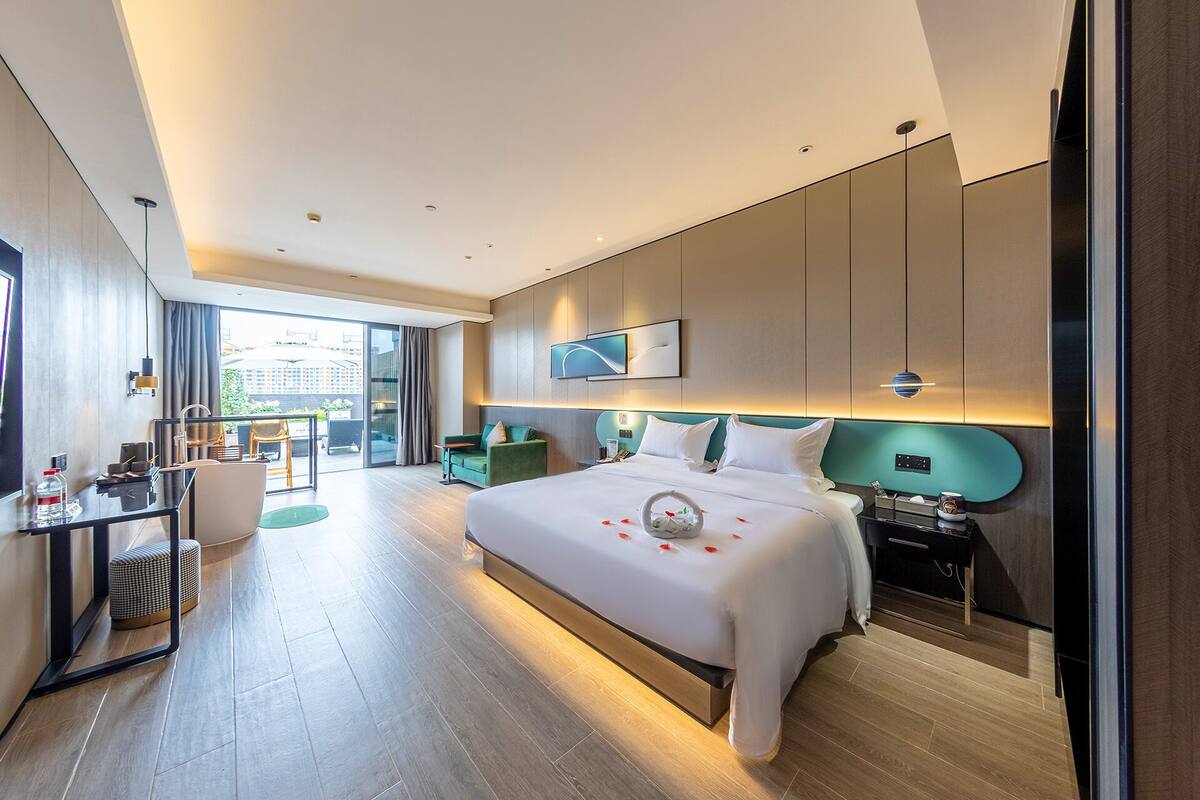 A modern hotel room with a large bed, a desk, a chair, and a view of the city.