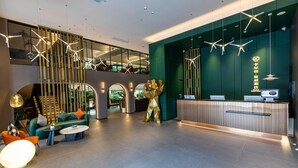 Un moderno vestíbulo de hotel con mostrador de recepción, zona de estar y una escalera que lleva a un nivel superior.