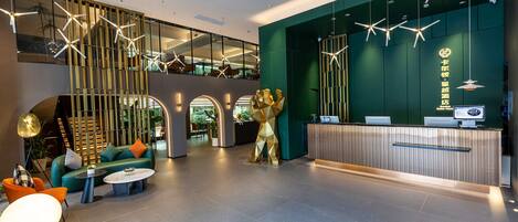 A modern hotel lobby with a reception desk, seating area, and a staircase leading to an upper level.