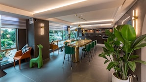 Un interior moderno con una zona de bar, sillas verdes, una mesa redonda y ventanas amplias.