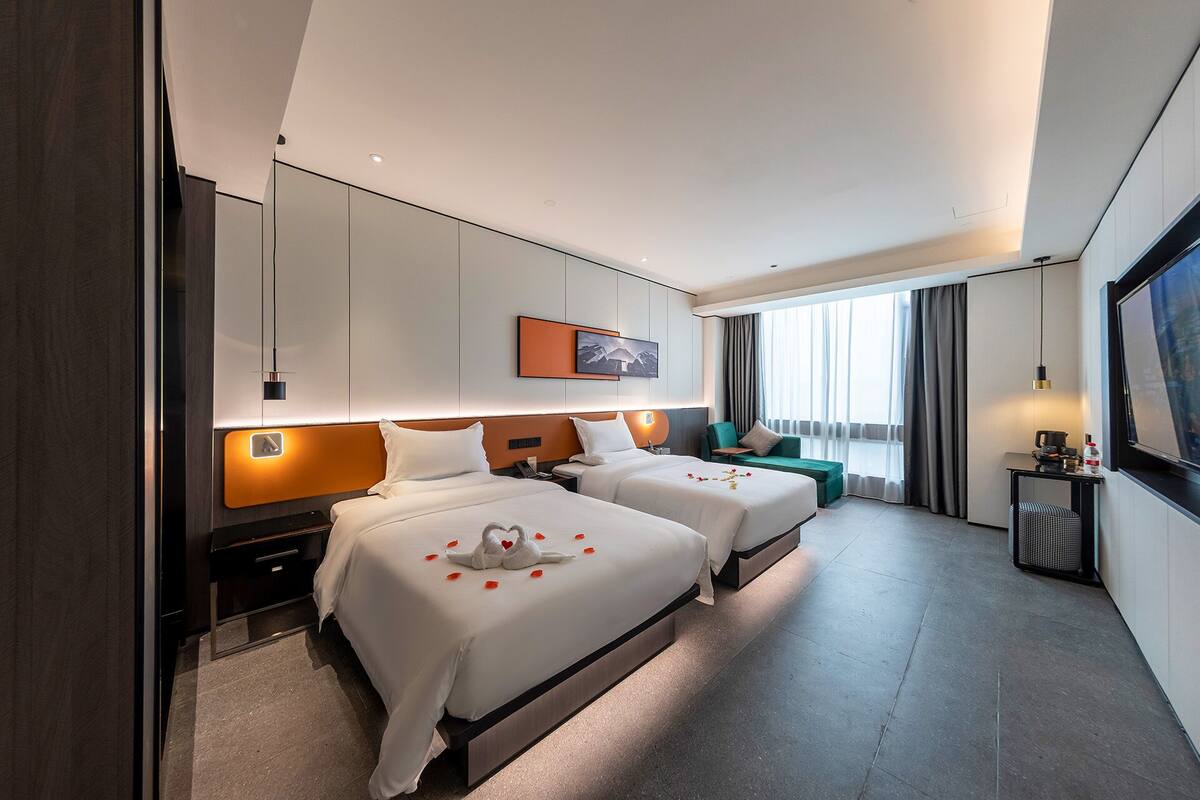 A hotel room with two beds, a sofa, a desk, and a TV.