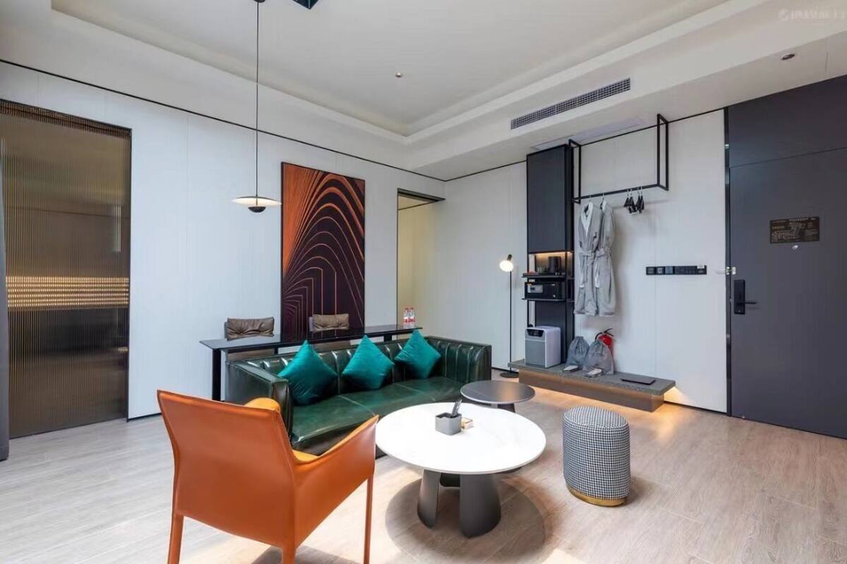 A modern living room with a green sofa, orange chairs, a round table, and a checkered ottoman.