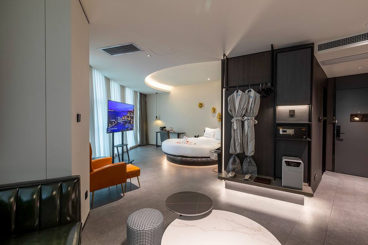 A modern hotel room with a bed, a TV, a robe, and a minibar.