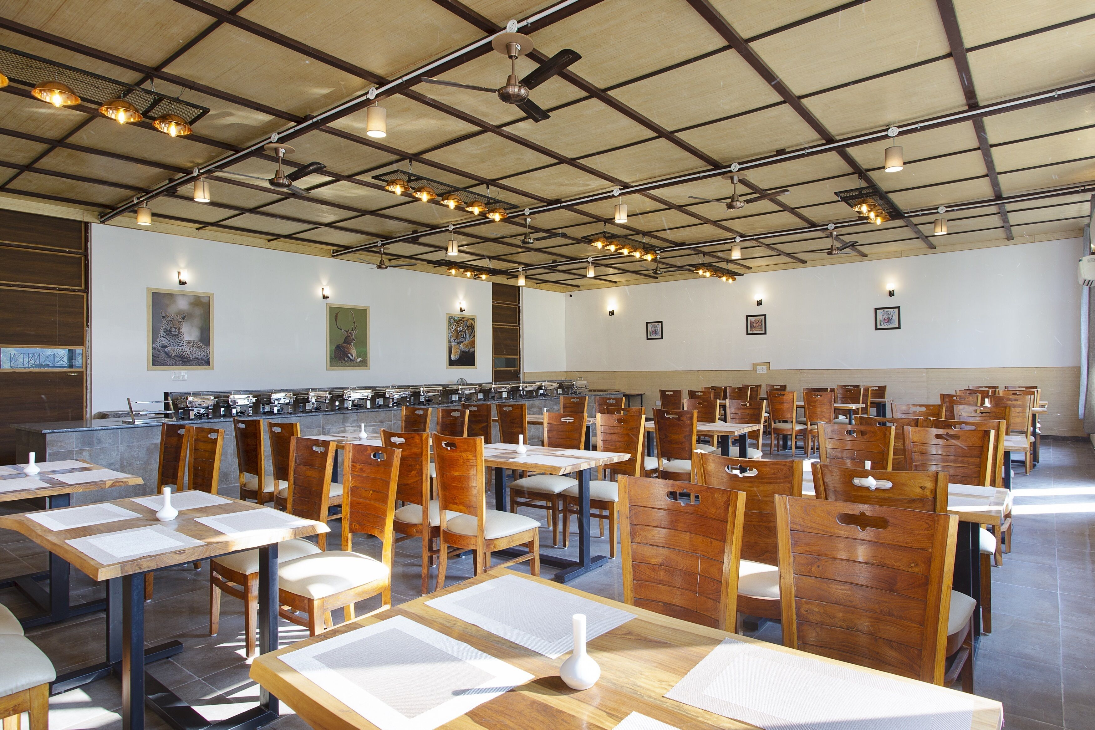 A spacious dining area with multiple tables and chairs, a long counter with a coffee station, and a high ceiling with exposed beams and lighting fixtures.
