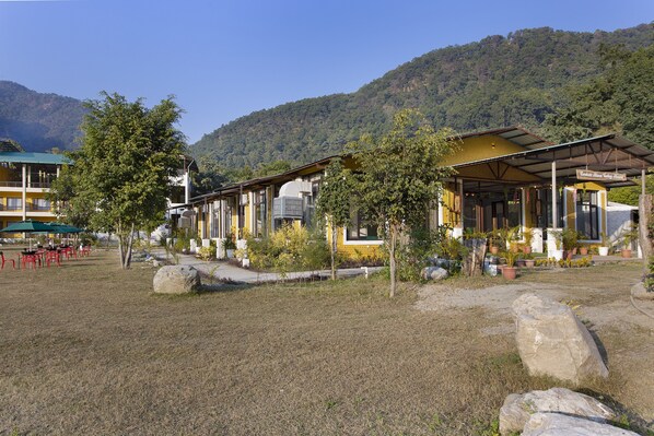 A yellow building with a covered outdoor seating area, surrounded by trees and large rocks.
