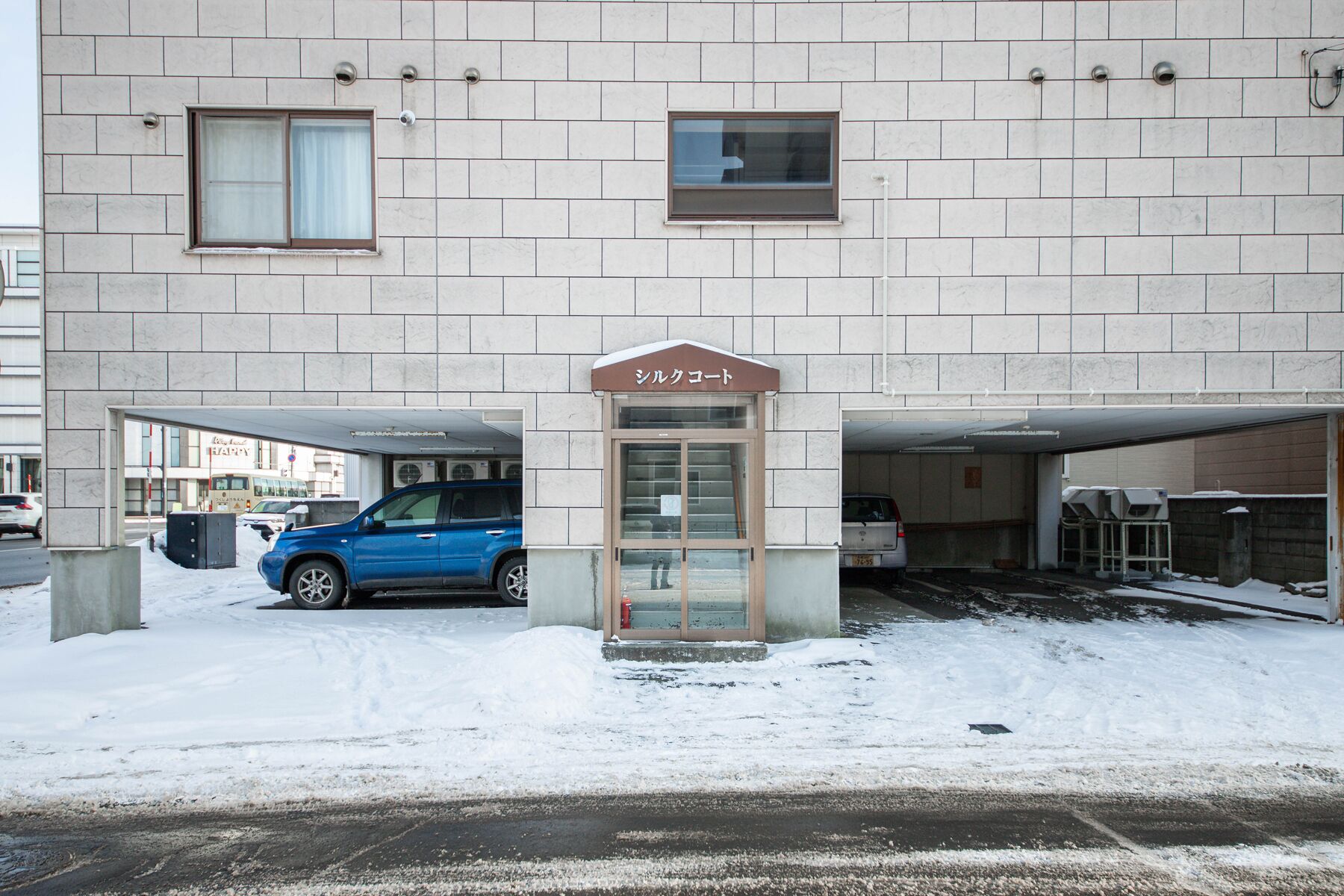 A building with a sign reading "Shulcoot" and a blue car parked in front.