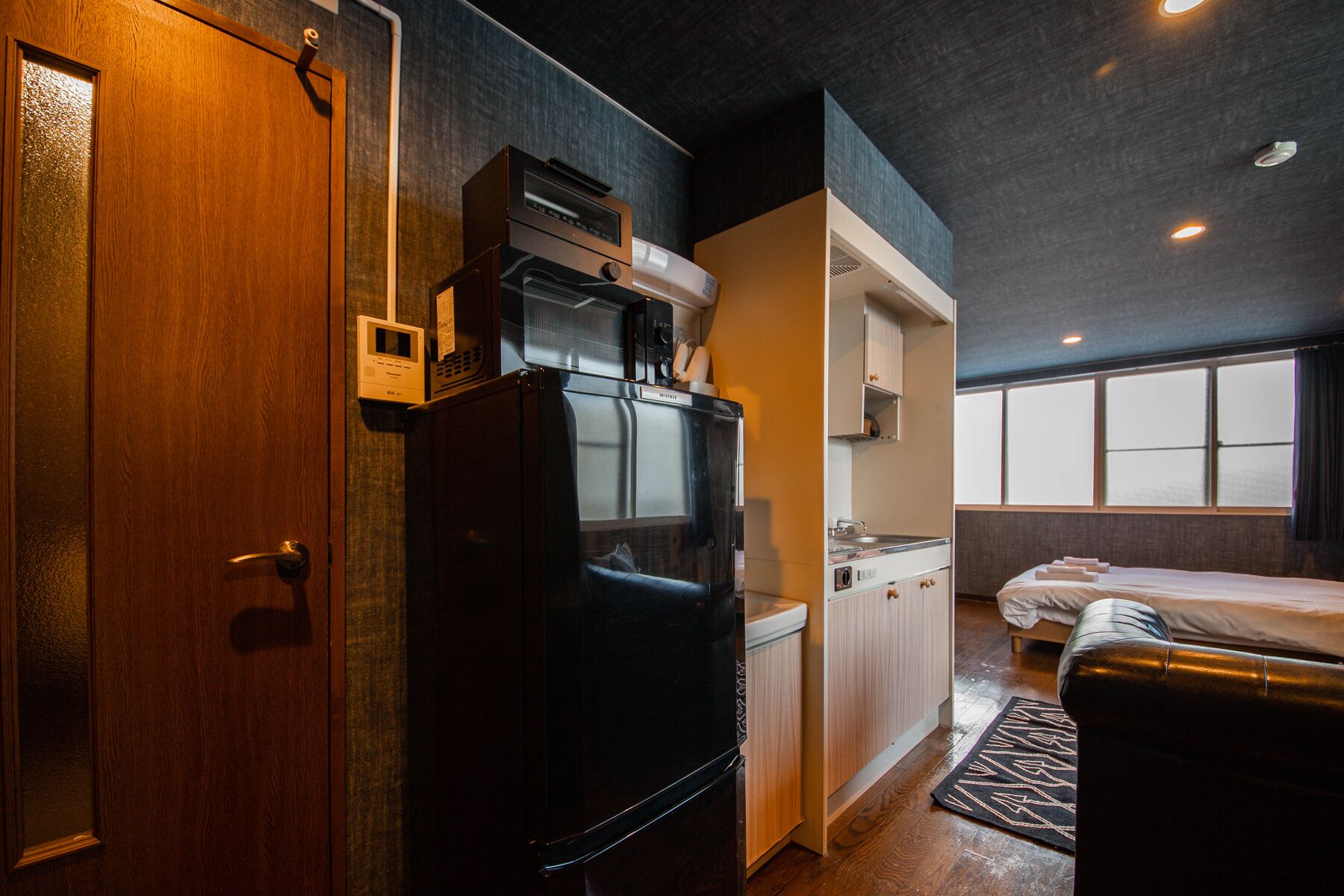 A compact hotel room with a kitchenette, a bed, and a large window.