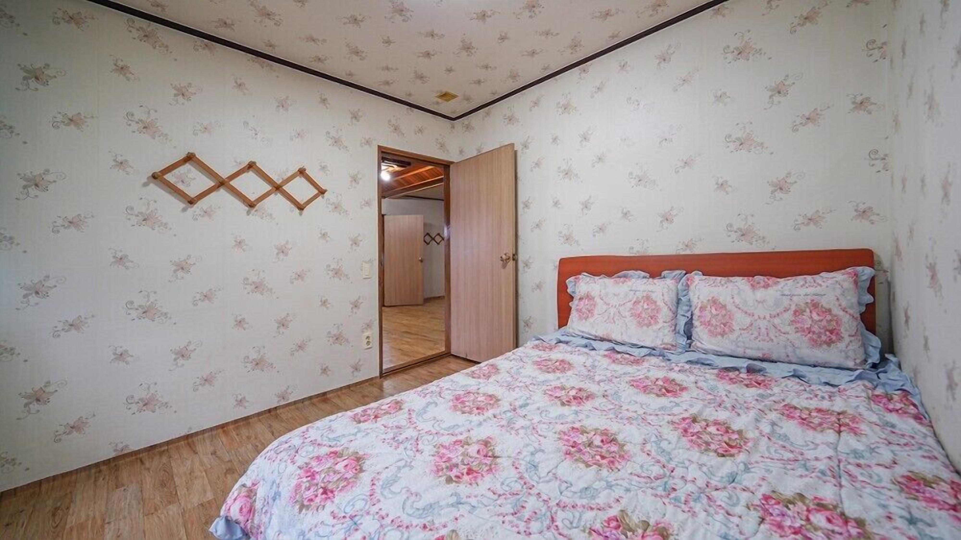 A bedroom with floral wallpaper, a wooden bed frame, and a mirror on the wall.