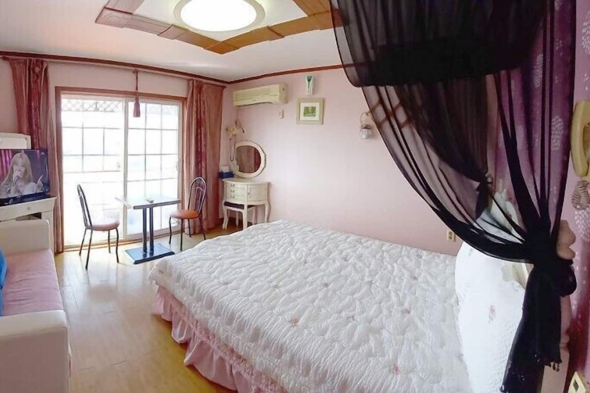 A bedroom with a bed, a sofa, a television, a table, and a chair.