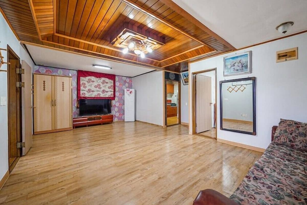 A spacious living area with wooden flooring, a sofa, a TV, and a wardrobe.