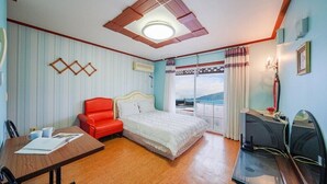 A hotel room with a bed, a red chair, a desk, a TV, and a balcony with a view. - Mangyang Full House (Geoje)