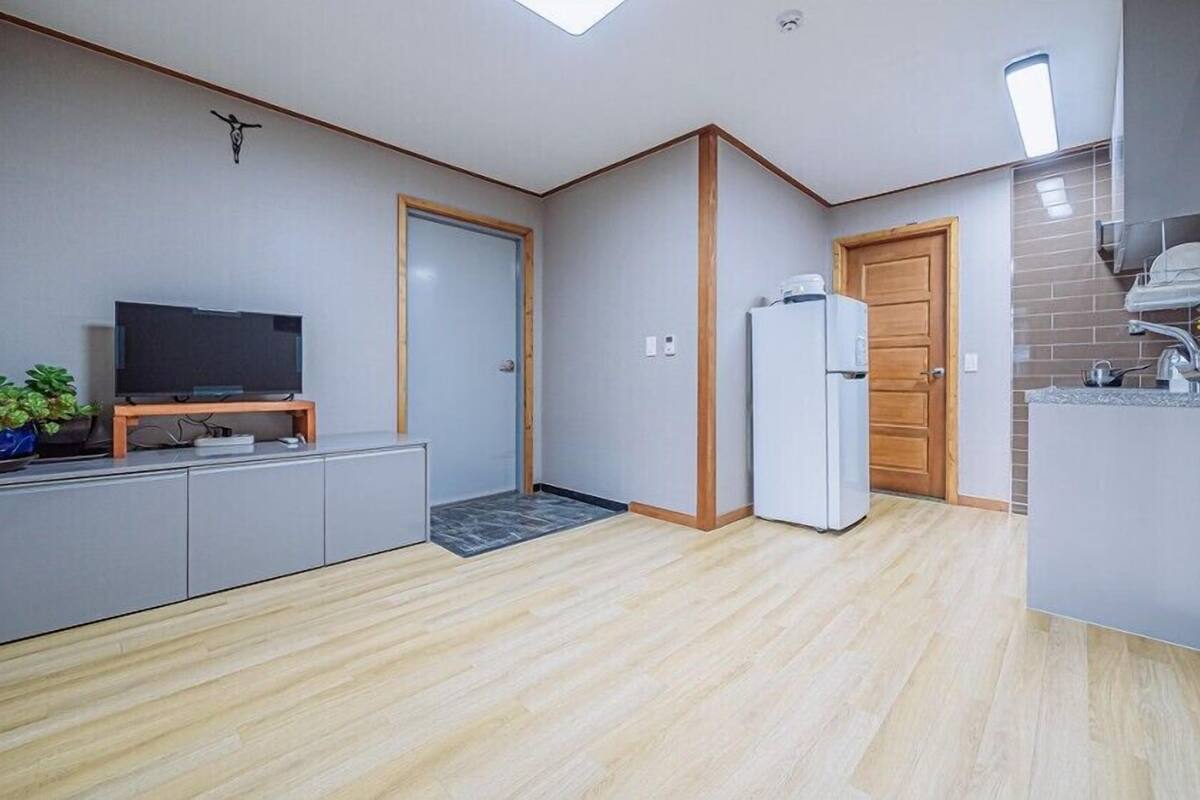 A compact living space with a kitchenette, a television on a wooden stand, and a refrigerator.