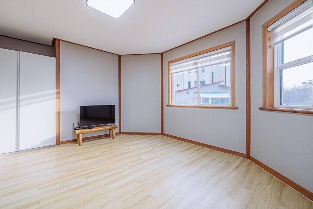 A room with a wooden floor, a TV on a small stand, and a window with blinds.