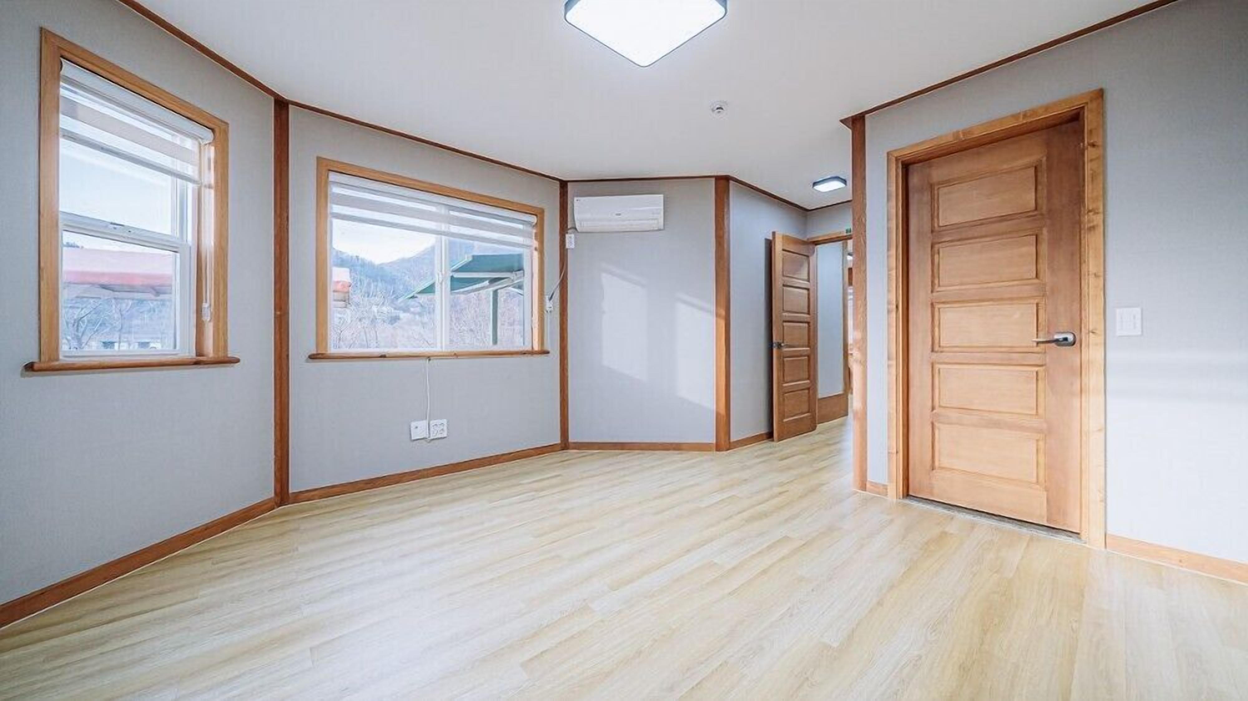 A room with wooden flooring, large windows, and a door.