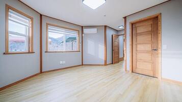 A room with wooden flooring, large windows, and a door.