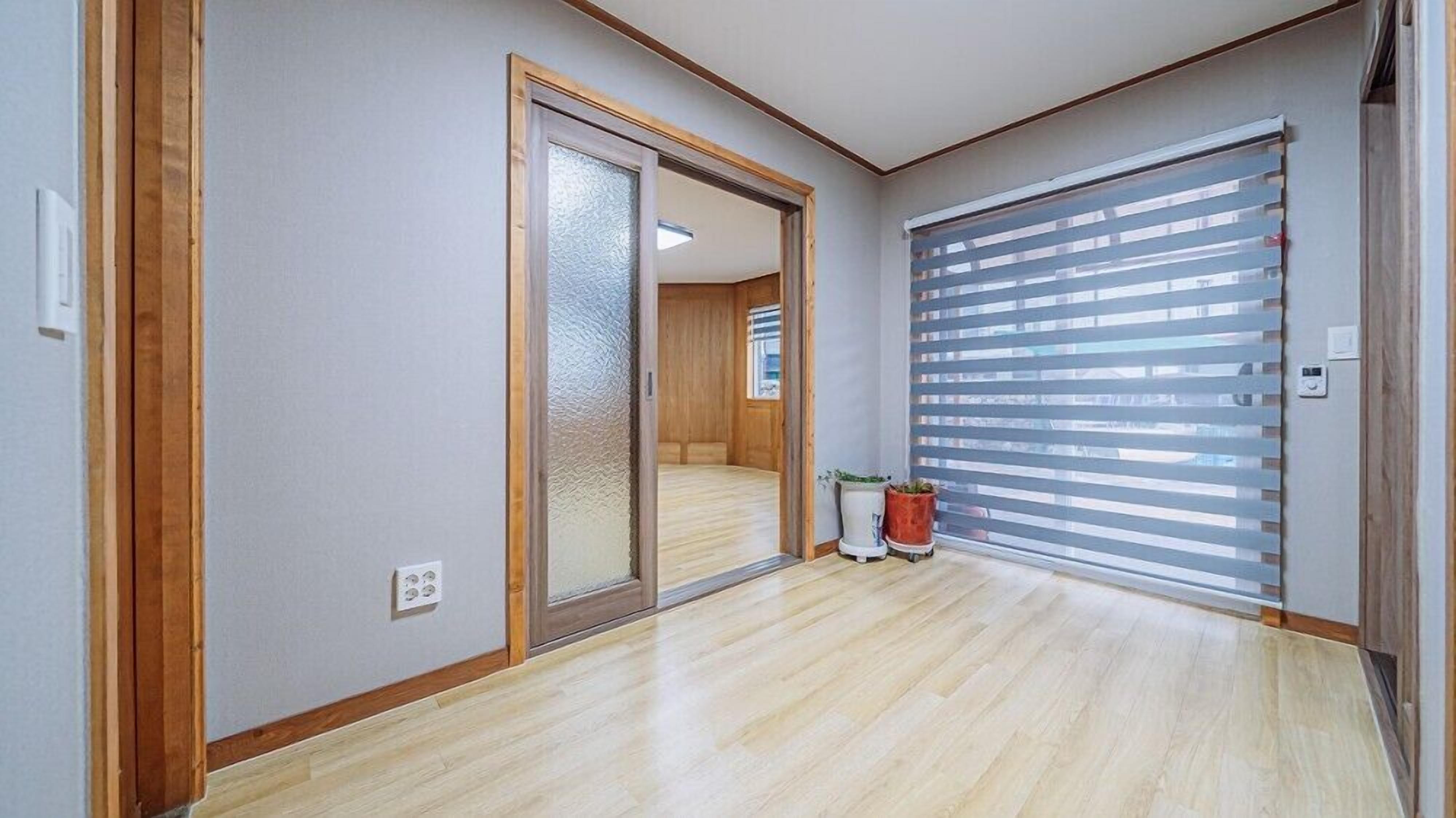 A hallway with a sliding glass door leading to a room, a potted plant, and a window with blinds.