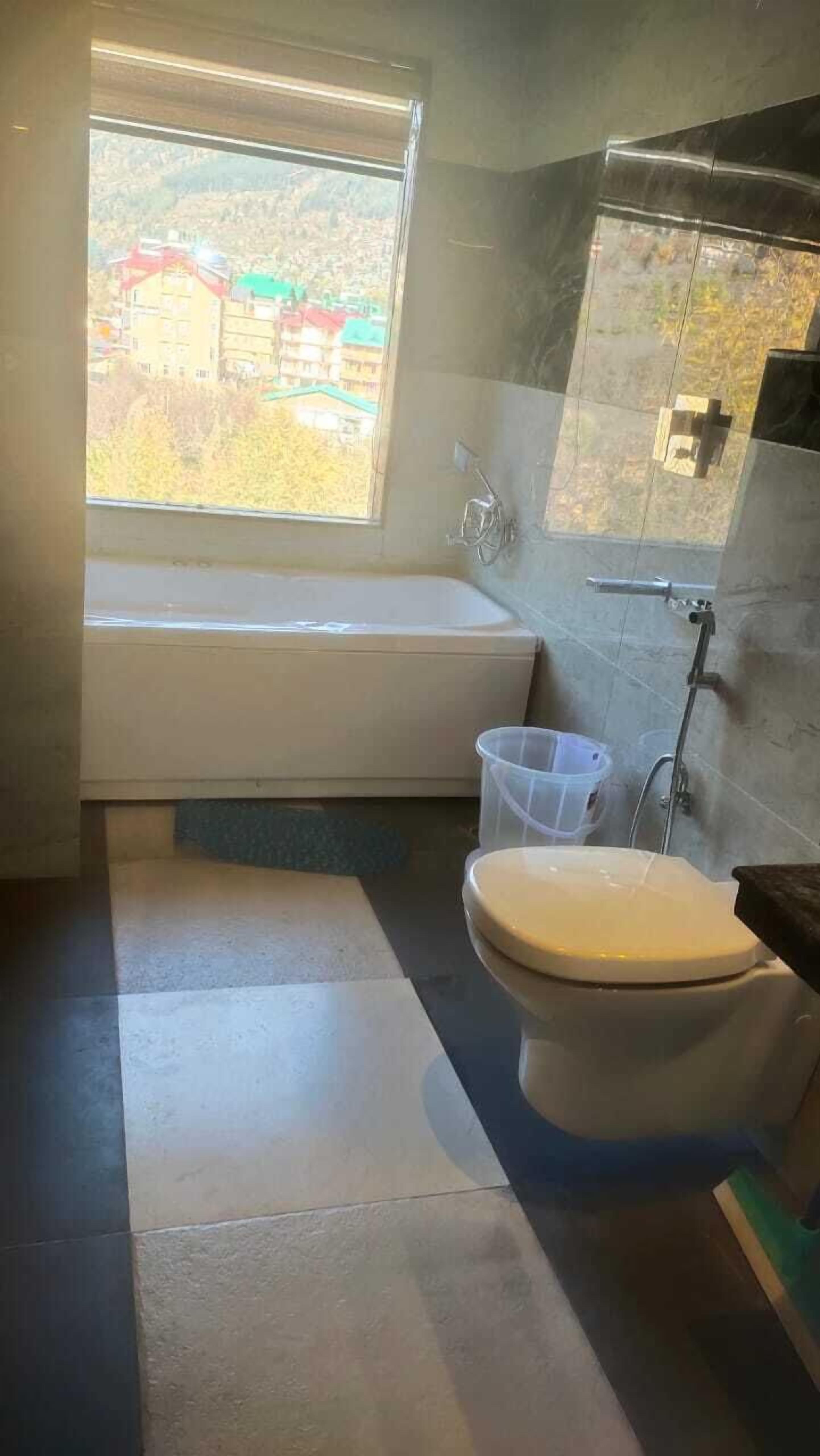 A bathroom with a bathtub, toilet, and a window with a view of buildings.