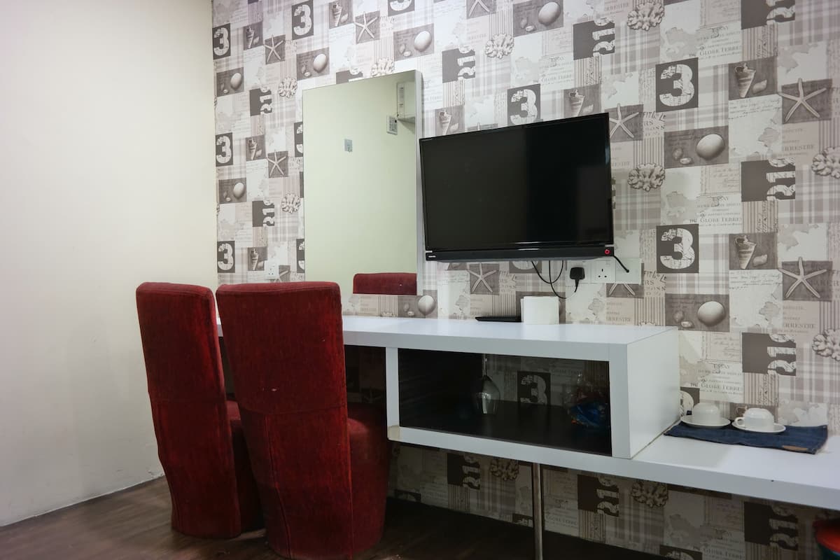 Una habitación con un televisor montado en la pared, una consola blanca y dos sillas rojas.