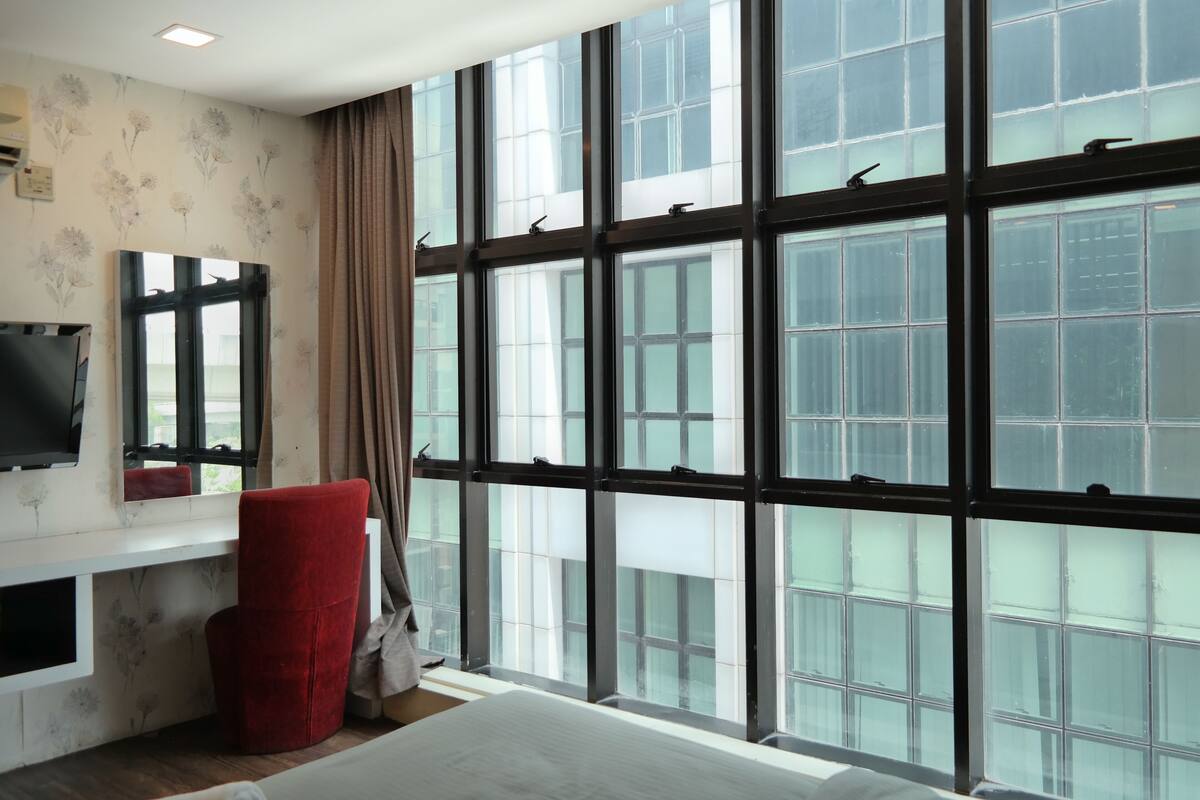 Una habitación de hotel moderna con ventanas amplias, una silla roja, un televisor de pantalla plana y una cama blanca.