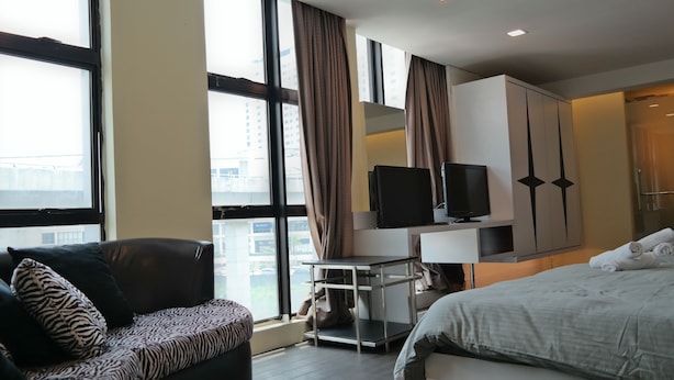 Una habitación de hotel moderna con una cama grande, un sofá, un televisor sobre un mueble bajo y un escritorio.