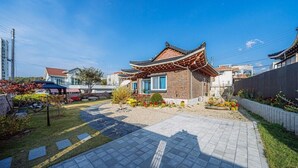 A traditional Korean-style house with a tiled roof, surrounded by a garden with various plants and a paved walkway. - dal geulim goun (Chuncheon)