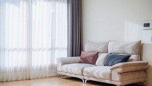 A modern living room with a beige sofa, a grey curtain, and a white wall. - dal geulim goun (Chuncheon)