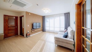 A spacious living room with a wooden floor, a sofa, a TV mounted on the wall, and a large window with curtains. - dal geulim goun (Chuncheon)