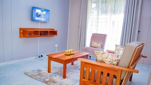 Una sala de estar con una mesa de centro de madera, un sofá, un televisor montado en la pared y una ventana con cortinas.