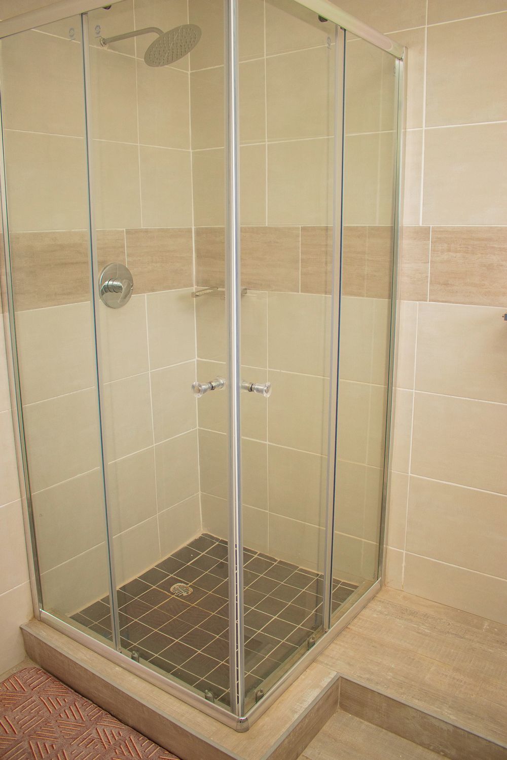 Une douche fermée par des parois de verre, avec un sol carrelé et une pomme de douche en métal.