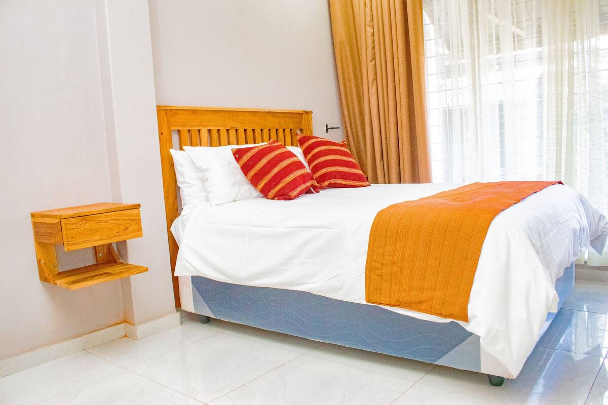 A neatly made bed with a wooden headboard, white bedding, and two red striped pillows.