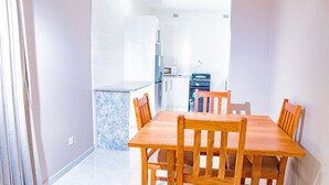 Un comedor con mesa y sillas de madera, una cocina al fondo y una ventana con cortinas.