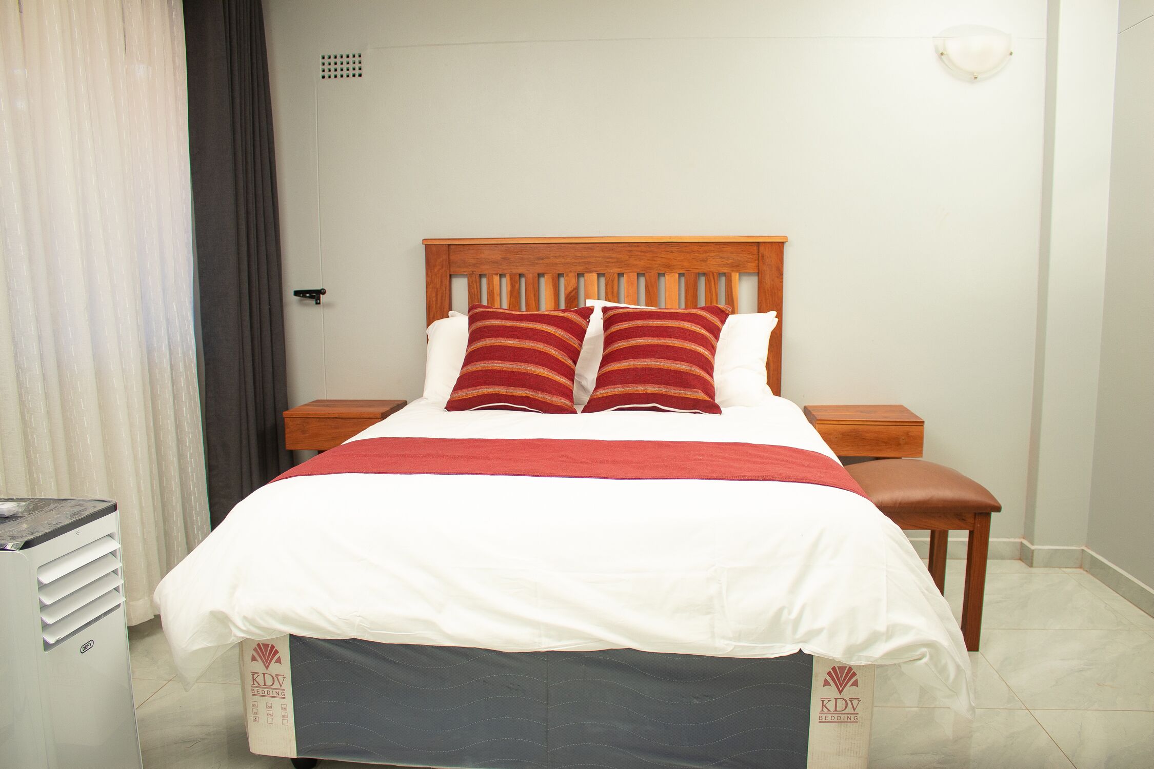Una cama bien hecha con cabecera de madera, dos almohadas y una colcha roja y blanca.