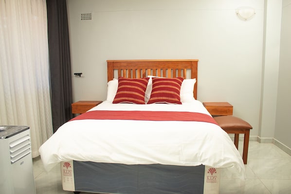 A neatly made bed with a wooden headboard, two pillows, and a red and white bedspread. - R Executive Apartments (Harare)