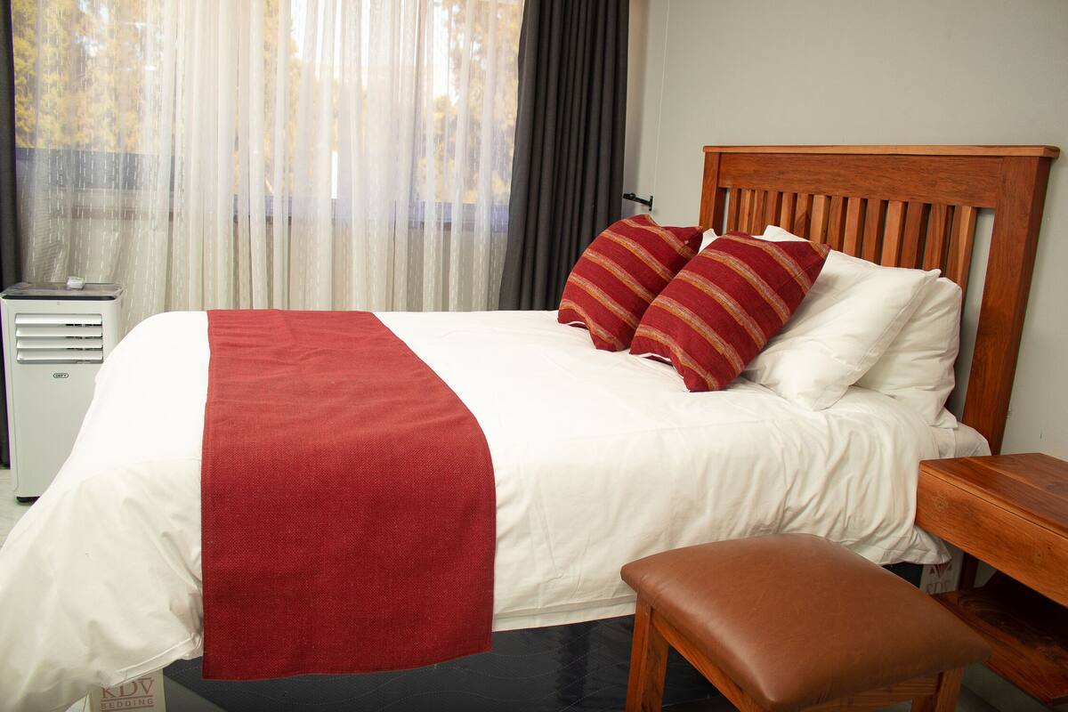 A neatly made bed with a wooden headboard, a red throw blanket, and two red pillows.