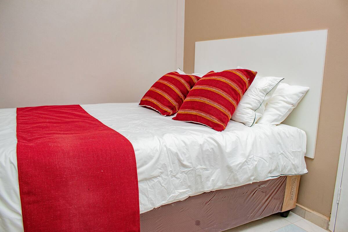 A bed with white bedding and red and yellow striped pillows, a red throw blanket, and a wooden headboard.
